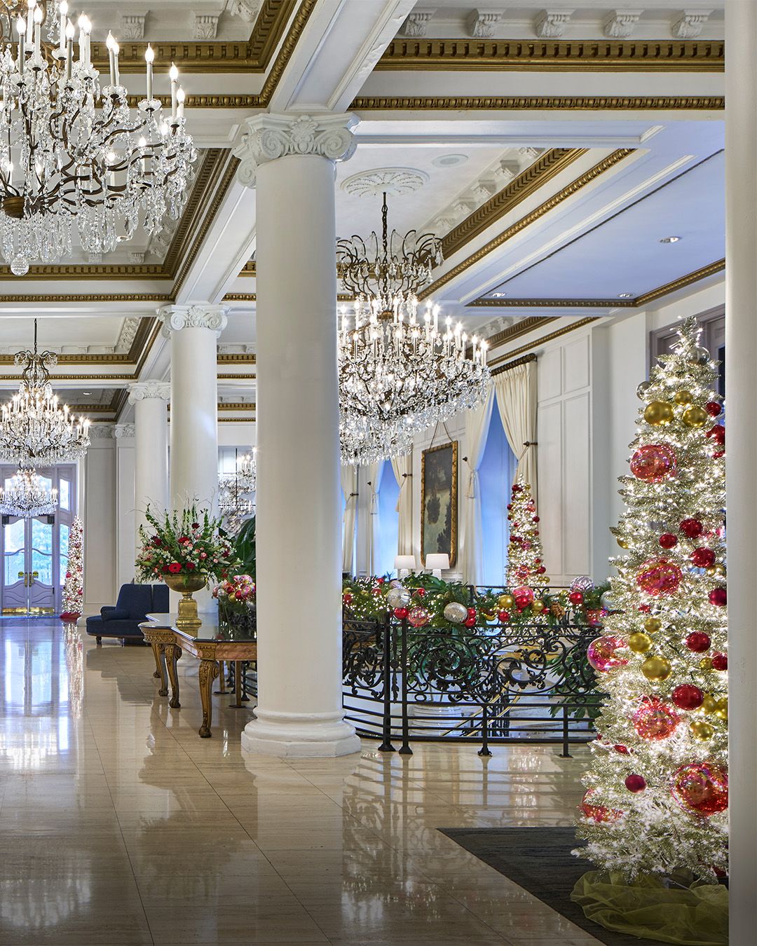 a large white room with a decorated tree and chandeliers